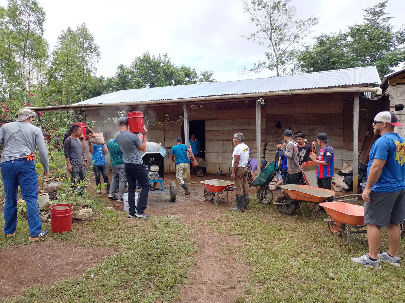 Volunteers with wheelbarrows gather outside a village home