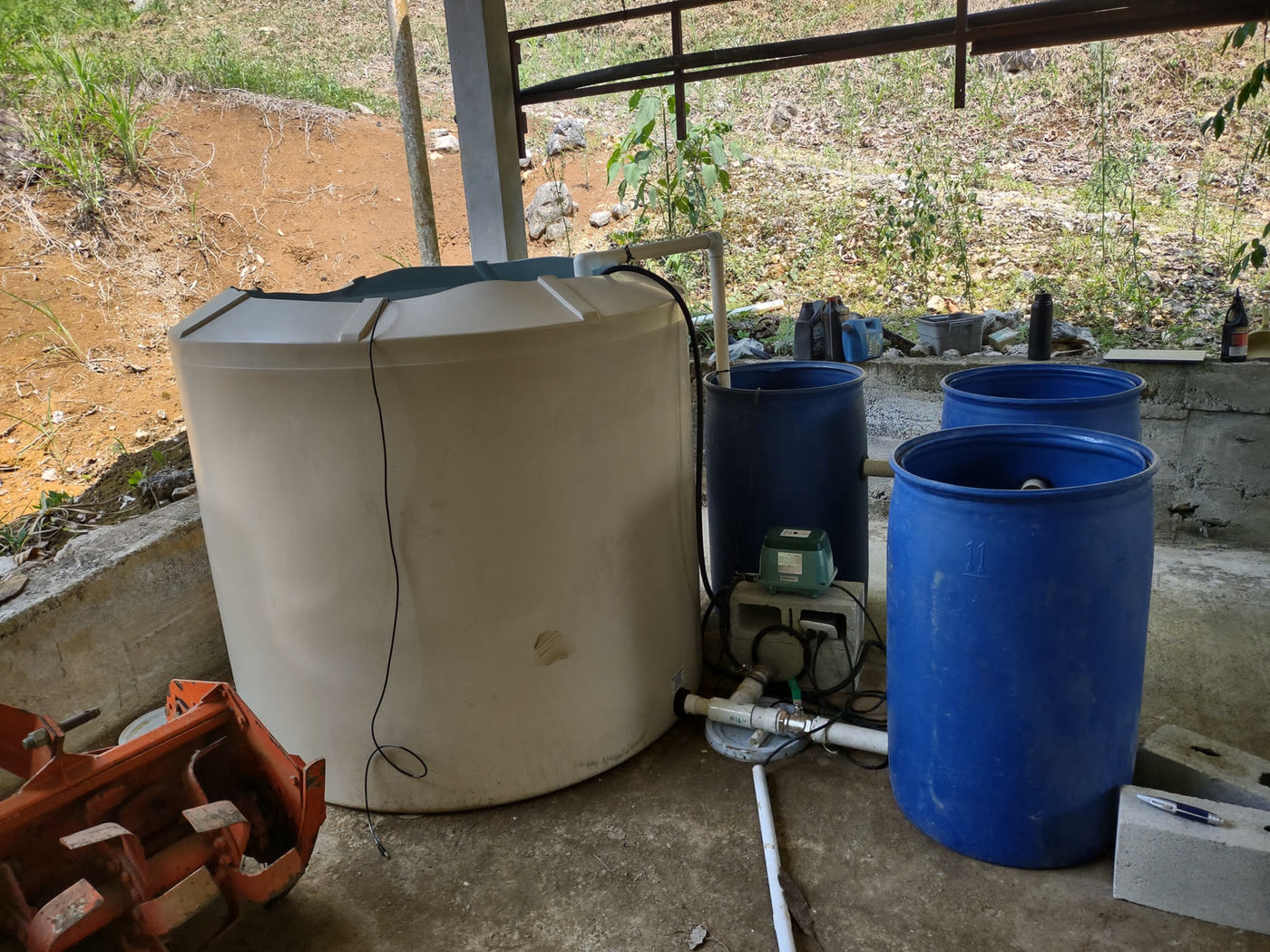 Water storage tanks and blue barrels under a shelter