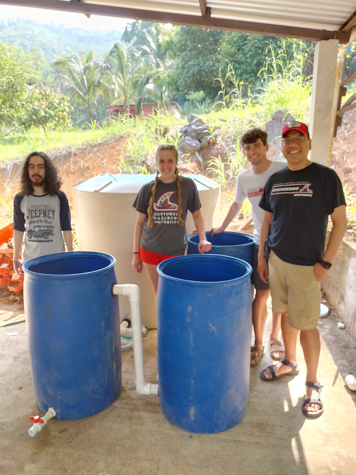Volunteers stand beside blue water barrels fitted with filters
