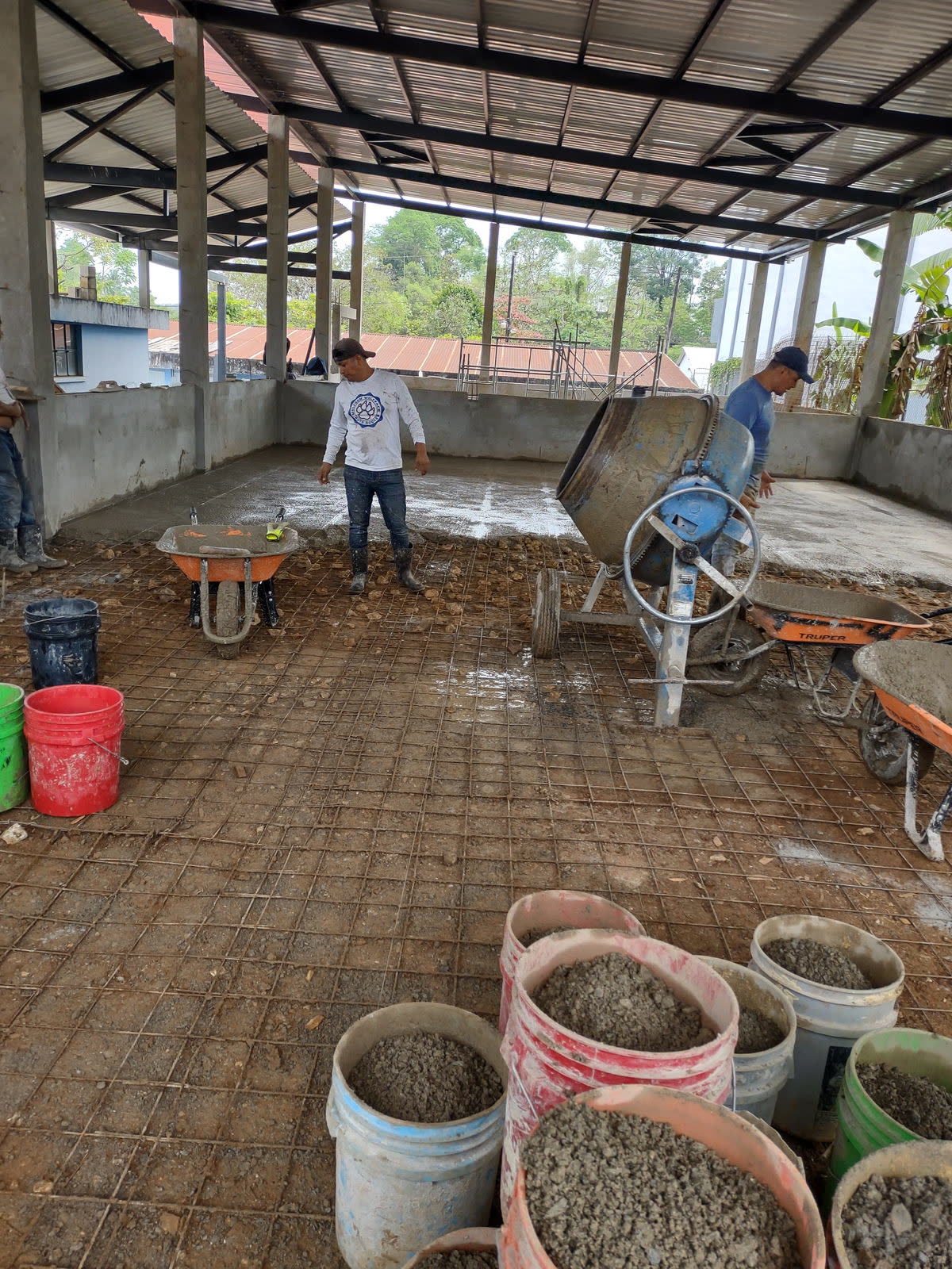 A reinforced concrete slab being prepared under a new roof, with buckets of gravel