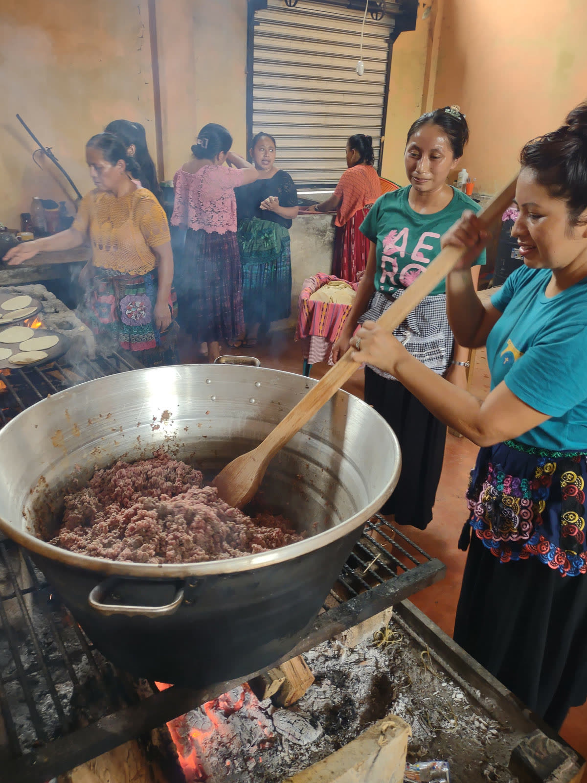 Women stir a large pot over an open fire