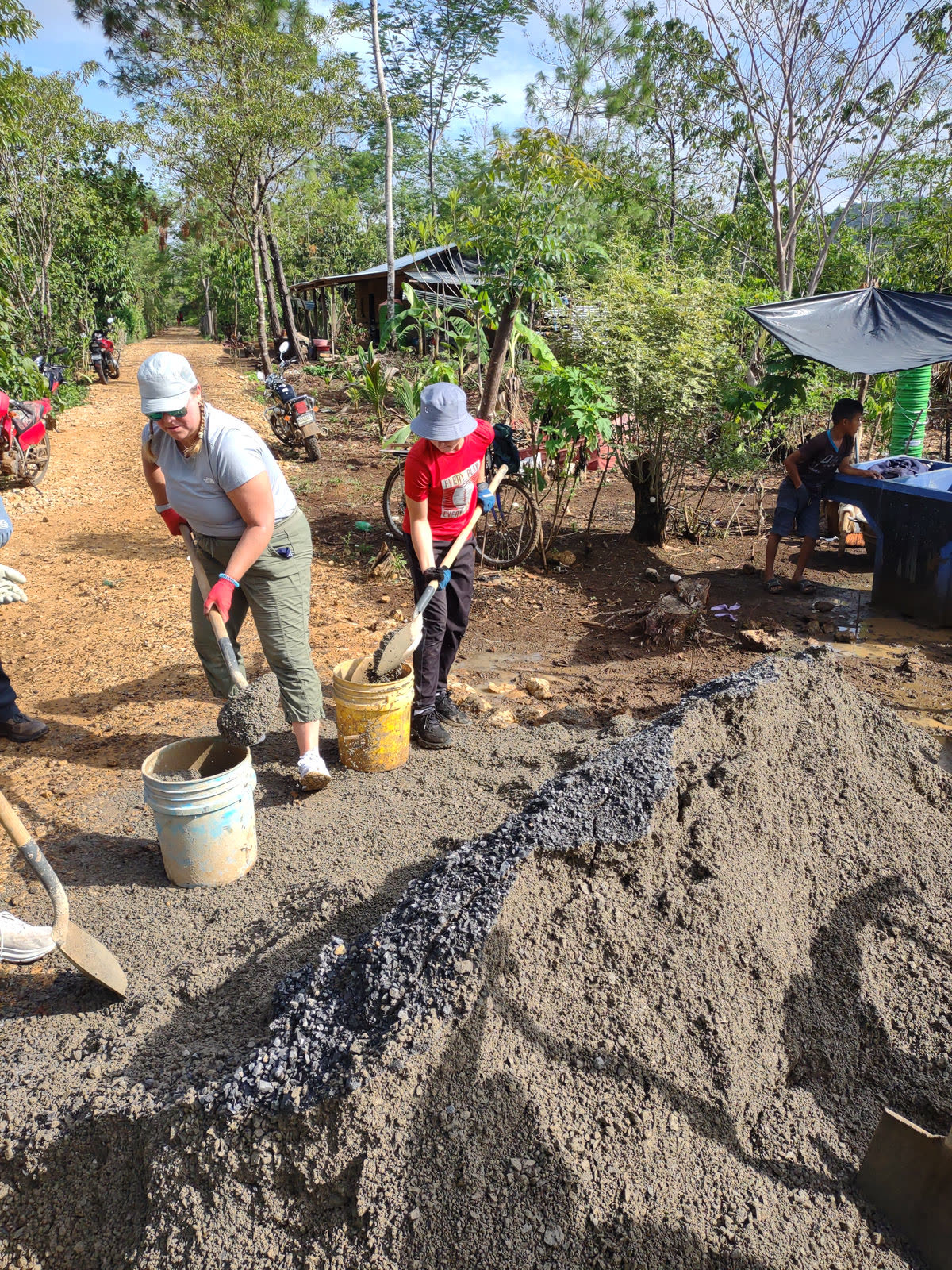 Volunteers dig with shovels beside a pile of gravel