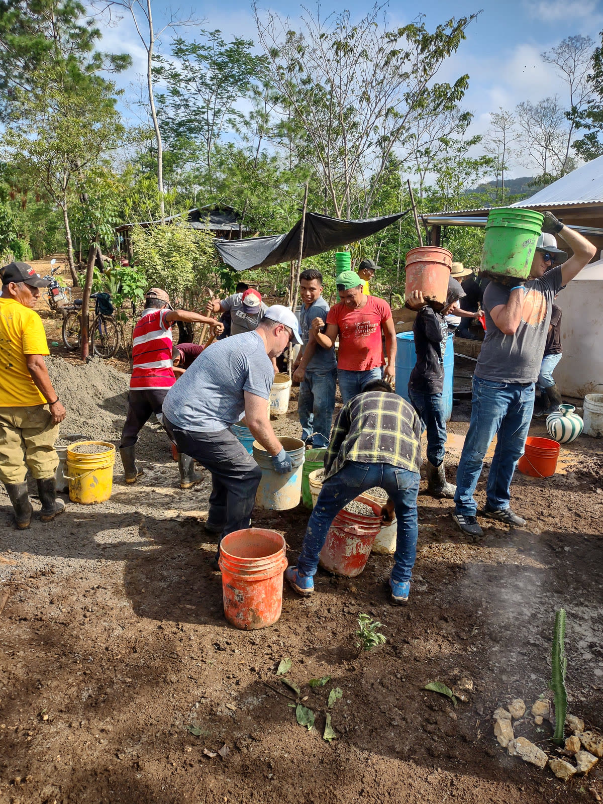 A group mixes concrete and carries buckets outdoors