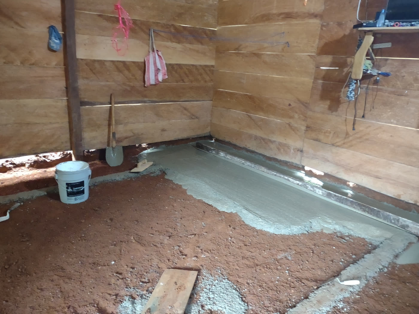 Fresh concrete being spread over the dirt floor inside a wooden home