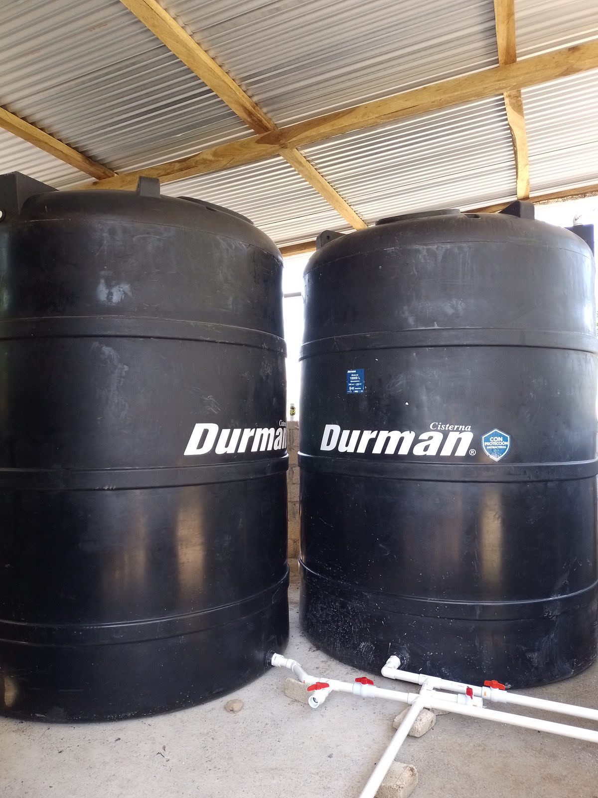 Two large black water storage tanks under a metal roof
